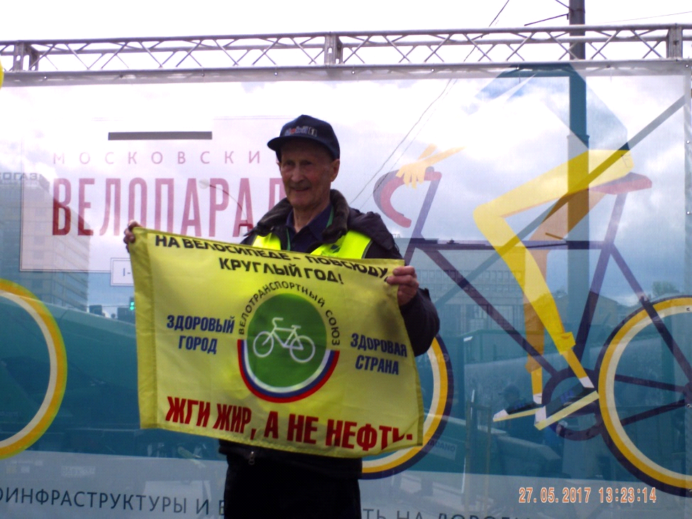 Геннадий Сергеевич Суздальцев с флагом ВТС и эмблемой Веломобильного центра на сцене под рев велотолпы, приветствующий 81-летнего велогладиатора.